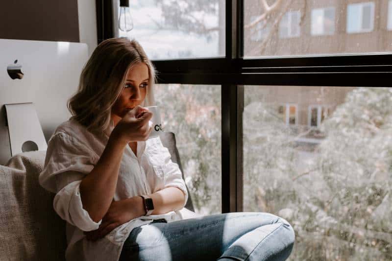 Frau hält eine weiße Tasse, die neben dem Fenster sitzt