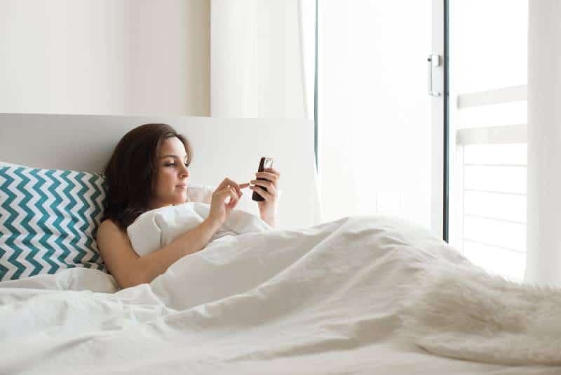 Frau im Bett, die soziale Apps mit Smartphone prüft