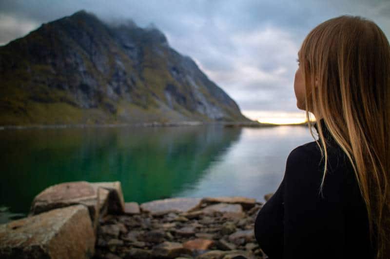 Frau in der schwarzen Jacke sitzt auf Felsen nahe See während des Tages