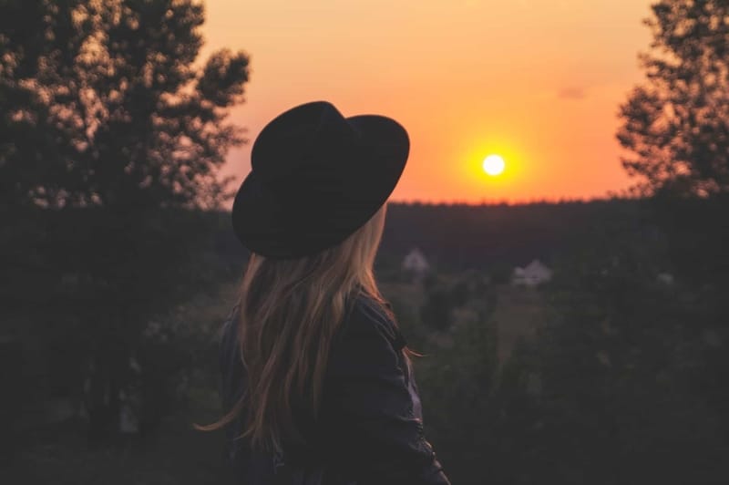 Frau mit Hut, die Sonnenuntergang beobachtet