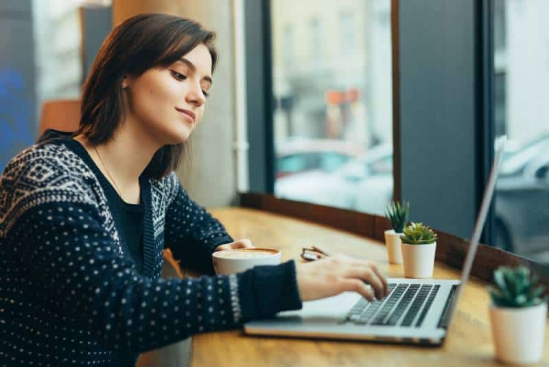 Frau schauen sich um und lächeln während der Arbeit im Cafe auf ihrem Laptop
