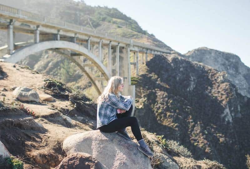 Frau trägt kariertes Hemd, das auf Felsen sitzt