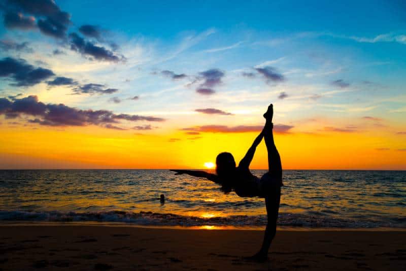 Gesunde Sportfrauen, die Yoga mit Meditation auf Strandsonnenuntergang tun