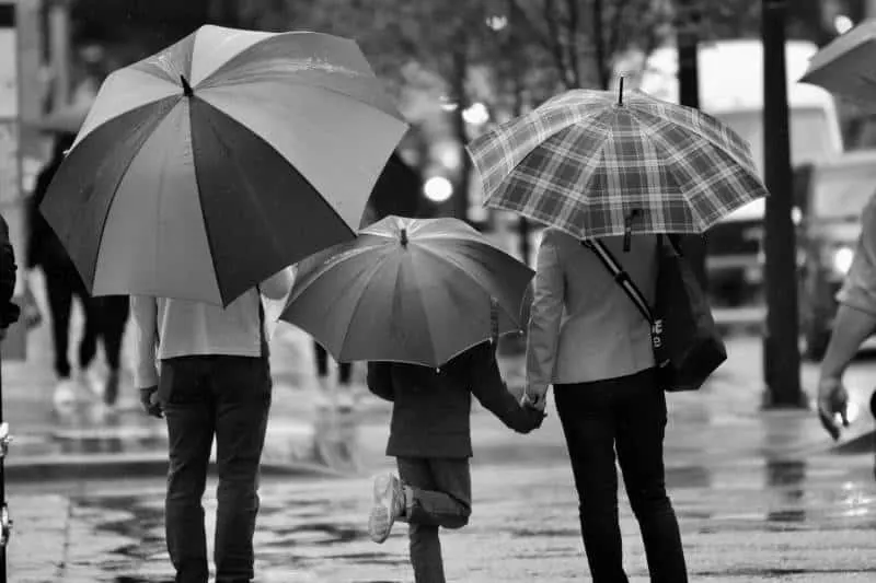 Graustufenfotografie von drei Personen mit Regenschirm