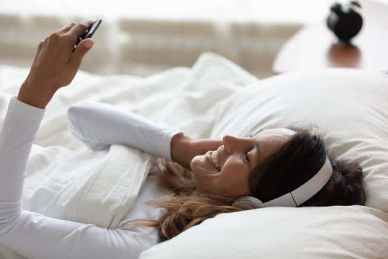 Hübsche Frau, die im Bett liegt, wacht nach dem Schlafen auf und fühlt sich glücklich