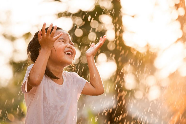 glückliches asiatisches Mädchen, das auf Regen steht