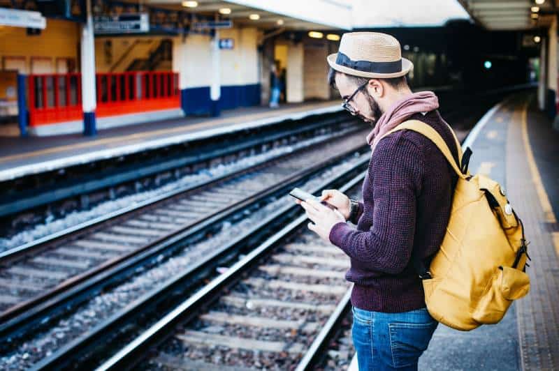 Mann, der Telefon benutzt, während er tagsüber vor Zugschiene steht