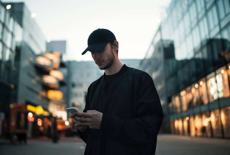 Mann in schwarzer Jacke mit schwarzer Mütze beim Telefonieren