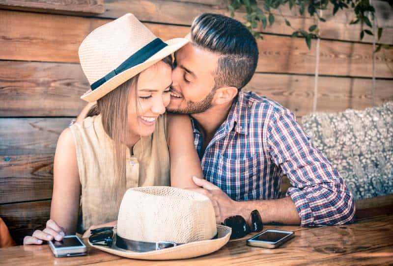 Mann küsst lächelnde Frau an der Wange am Kaffee