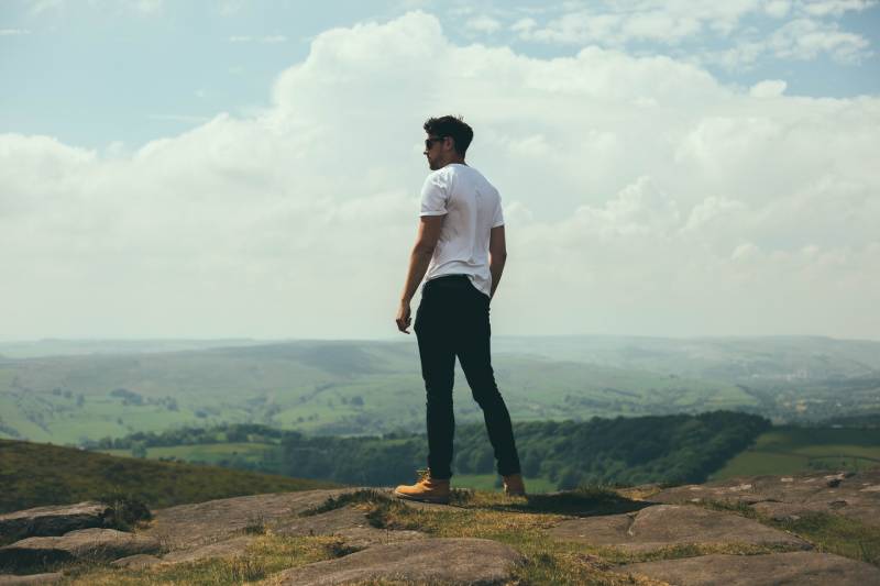 Mann stehend auf Felsbrocken mit Blick auf die Hügel und Berge