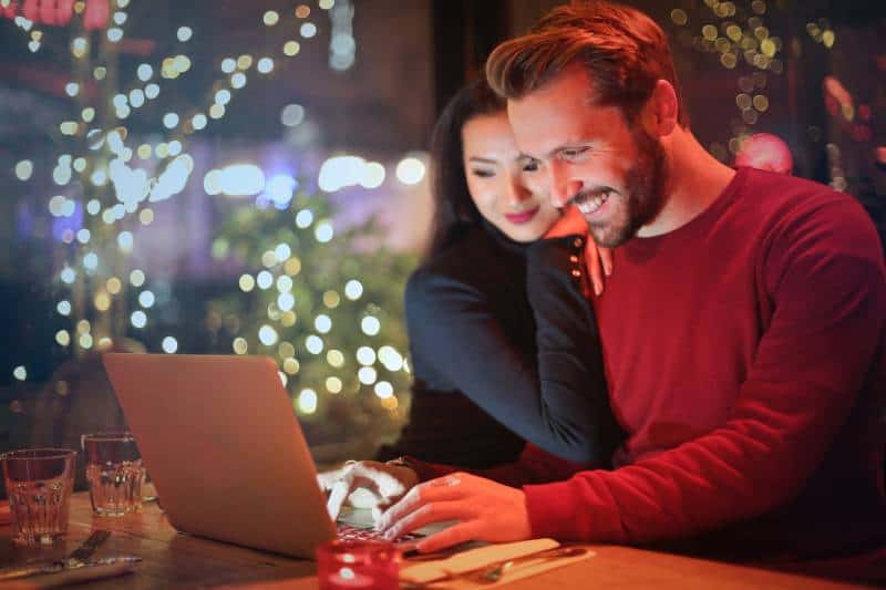 Mann und Frau, die auf silbernem Laptop beim Lächeln schauen