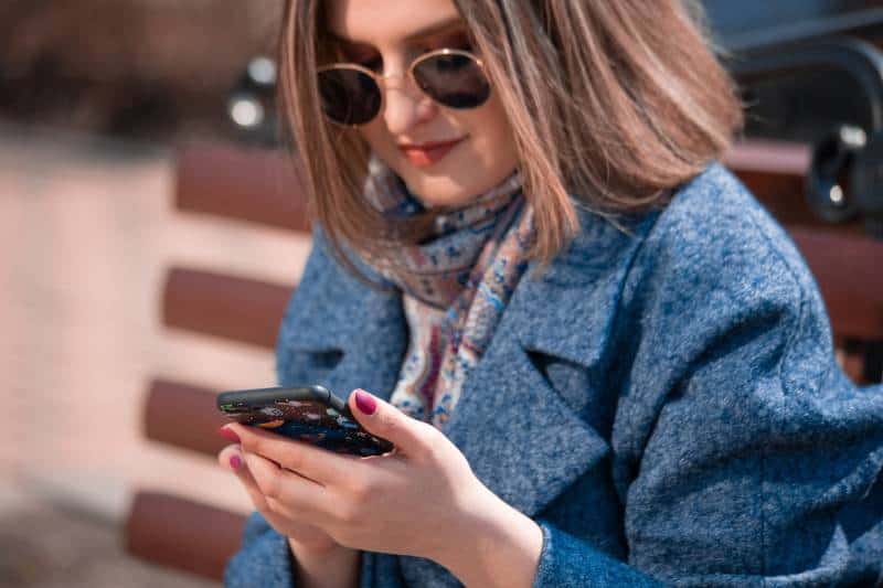 Mädchen, das auf ihrem Telefon tippt, während es auf Parkbank sitzt