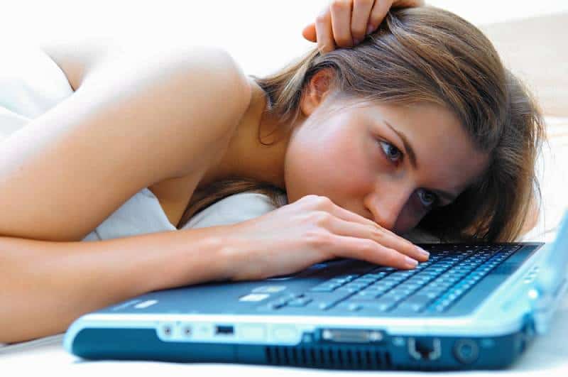 Mädchen im Bett liegen und auf Laptop tippen