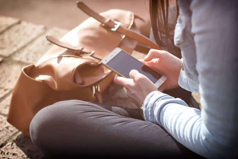 Mädchen sitzt auf Ziegeln und tippt eine SMS