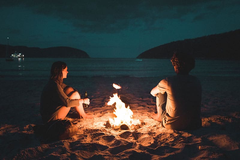Paar sitzt am Strand neben dem Feuer