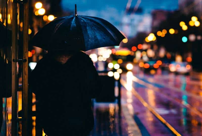 Person, die auf Straße geht, während schwarzer Regenschirm hält