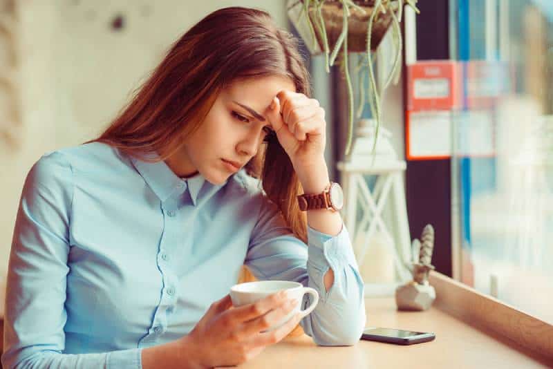 Porträt betonte traurige junge Frau mit Kaffeetasse, die am Café sitzt