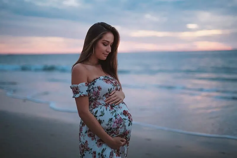 schöne schwangere Frau, die auf dem Sand steht