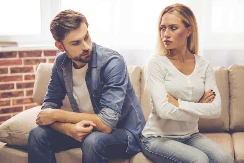 Schönes Paar sitzt Rücken an Rücken auf der Couch und schaut