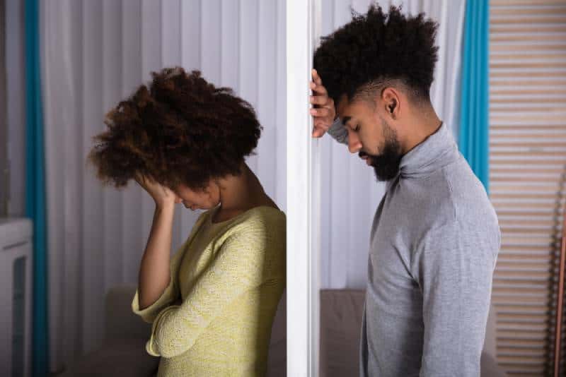 Seitenansicht des jungen unglücklichen Paares, das Rücken an Rücken zu Hause steht