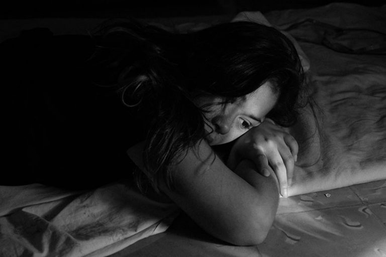 traurige Frau, die allein auf dem Bett liegt