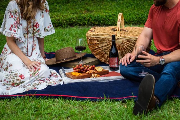 Mann und Frau sitzen auf blauem Textil neben braunem Weidenpicknickkorb