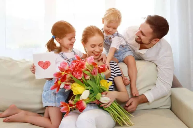 Vater und Kinder gratulieren der Mutter zum Urlaub und schenken Blumen