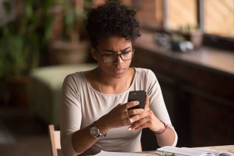 Verärgerte verwirrte afrikanische Frau, die Handy hält Problem hat