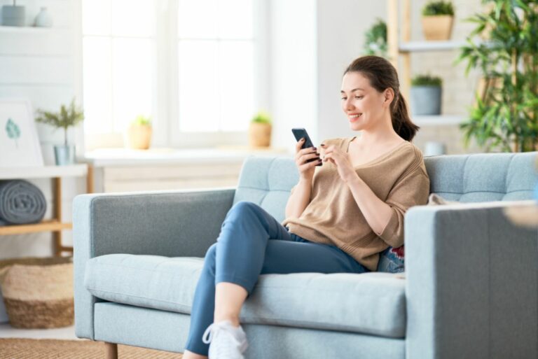 Ein schönes Mädchen sitzt auf der Couch und tippt am Telefon