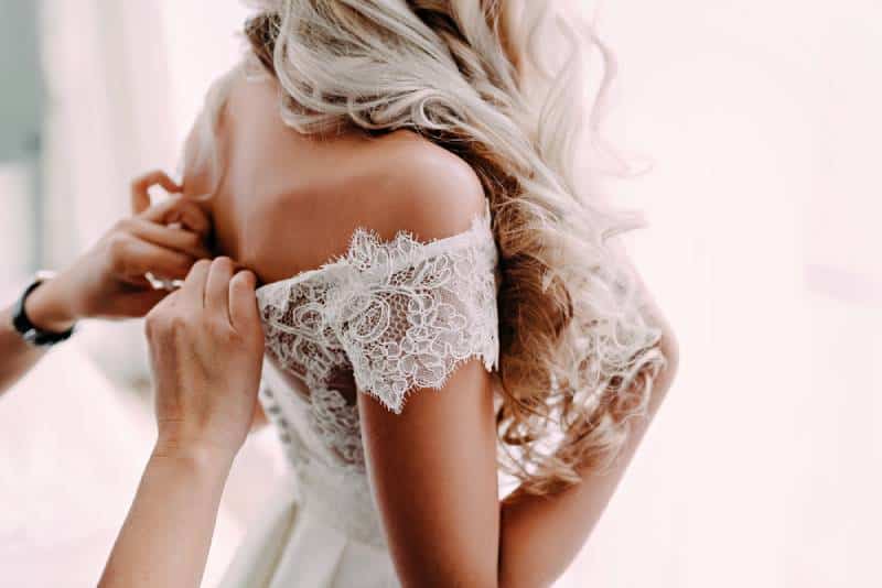 Wunderschöne, blonde Braut im weißen Luxuskleid bereitet sich auf die Hochzeit vor