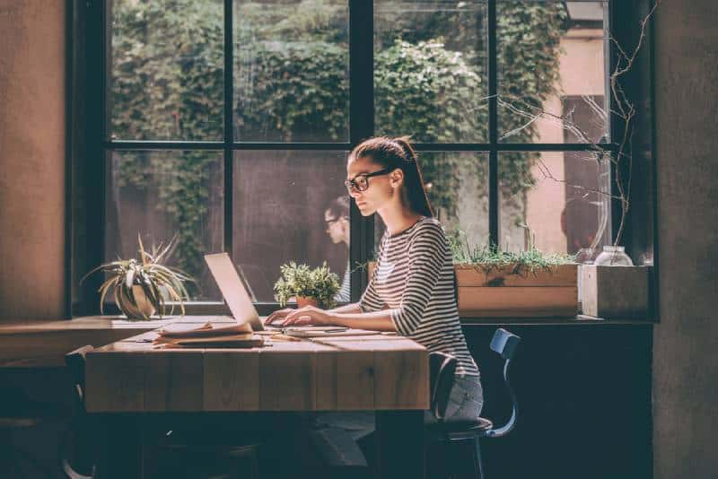 Zuversichtlich junge Frau in der intelligenten Freizeitkleidung, die am Laptop arbeitet