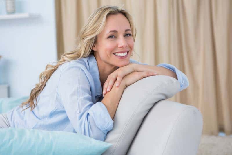 fröhliche hübsche Blondine sitzt auf der Couch zu Hause im Wohnzimmer