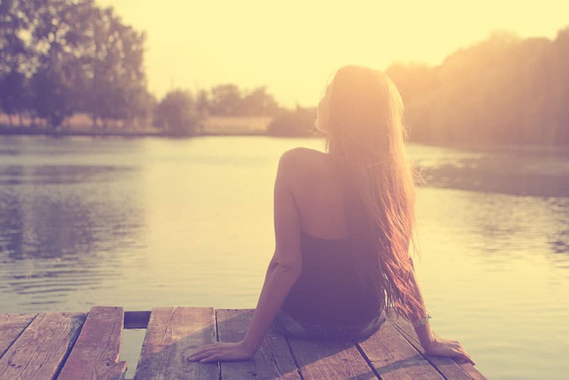 glückliche Frau, die am See sitzt