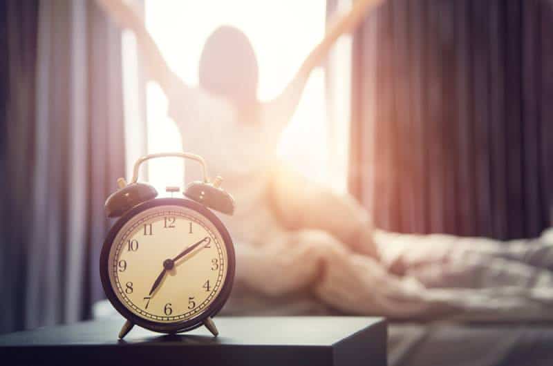 glückliche Frau, die sich nach dem Aufwachen im Bett ausdehnt, Sonnenlicht am Morgen