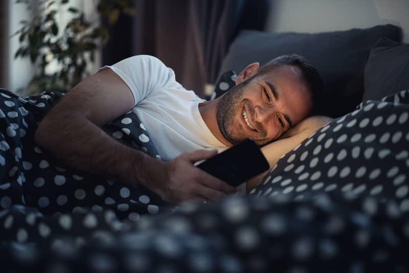 glücklicher Mann, der während der Nacht auf seinem Telefon tippt