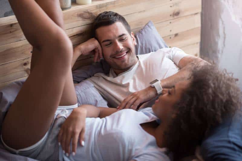 glückliches Paar auf dem Bett liegen und reden