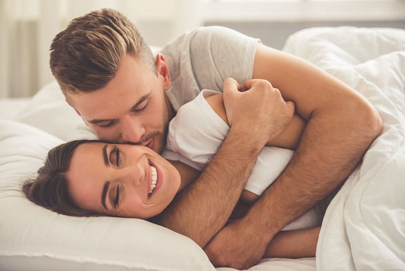 gutaussehender Mann, der seine Frau im Bett umarmt und küsst