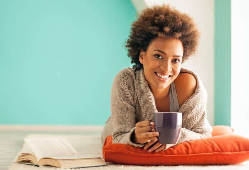 junge Frau, die eine Tasse Kaffee genießt, während sie zu Hause entspannt