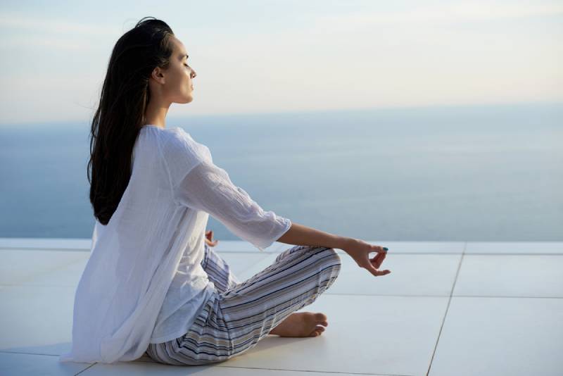 junge Frauen üben Yoga-Meditation auf Sonnenuntergang mit Meerblick im Hintergrund