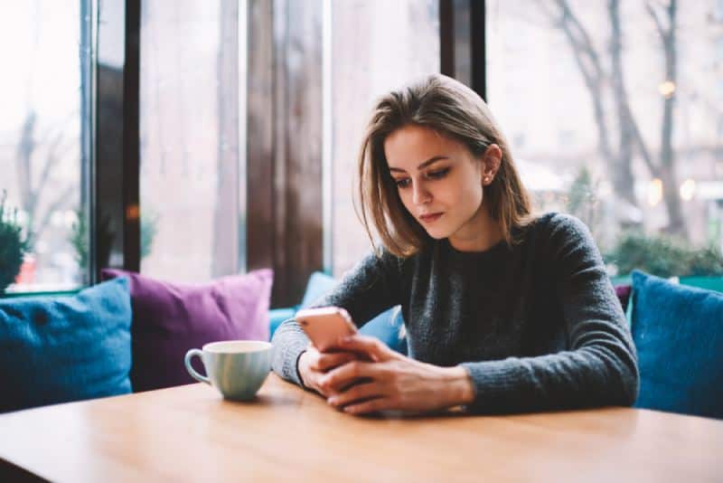 junges Mädchen, das an der Kaffeebar sitzt und Telefonbildschirm betrachtet