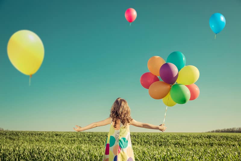 kleines Mädchen, das mit bunten Luftballons spielt