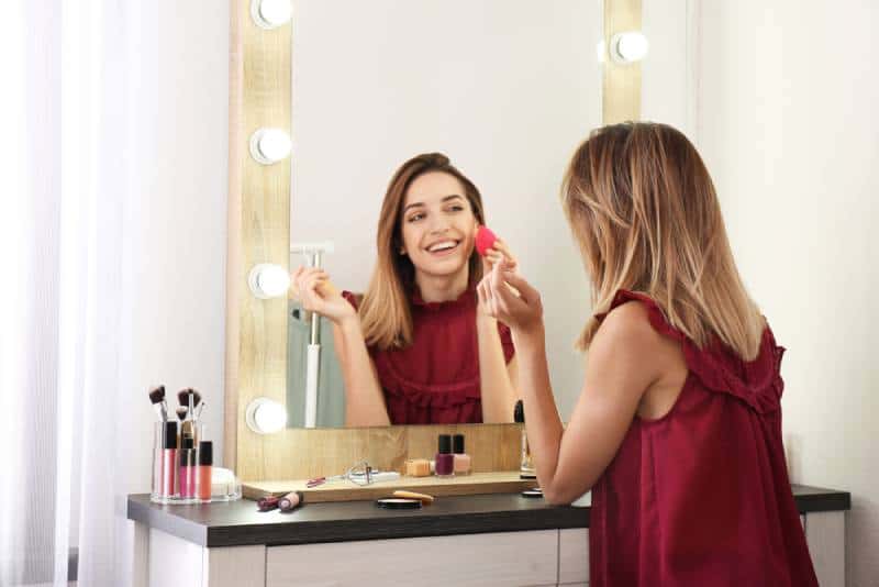 lächelnde Frau, die Make-up vor dem Spiegel anwendet