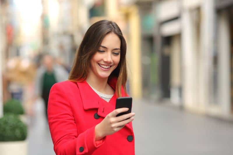 lächelnde Frau, die ihr Telefon auf der Straße betrachtet