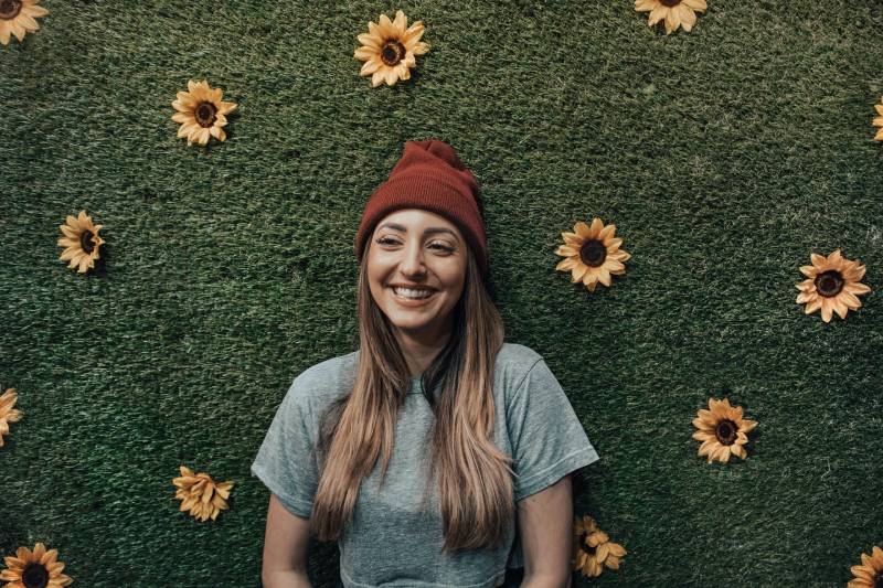 lächelnde Frau, die sich auf Blumenwand stützt