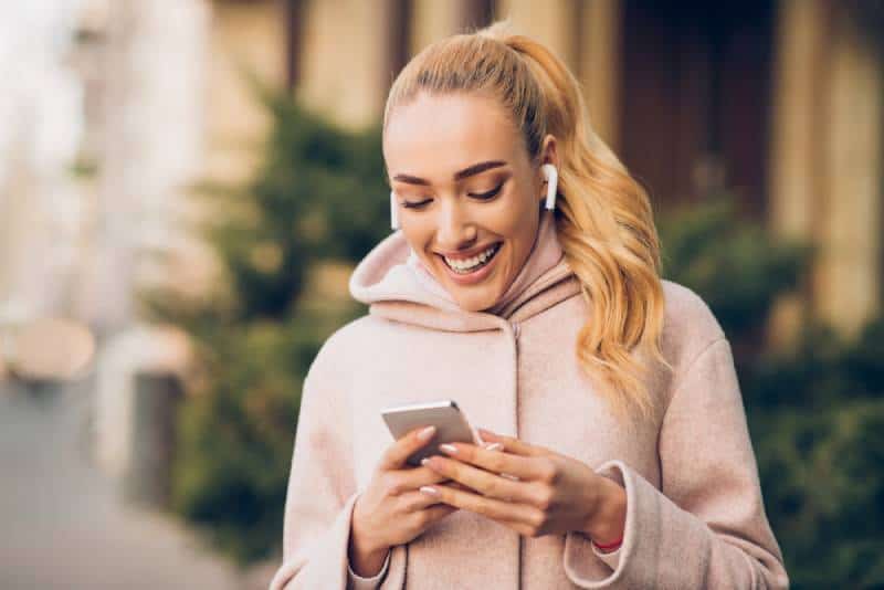 lächelnde Frau, die auf ihrem Telefon tippt und draußen Musik hört