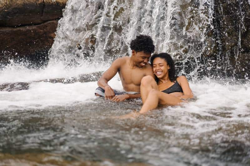 lächelnder topless Mann, der nahe seiner Freundin nahe Wasserfall sitzt