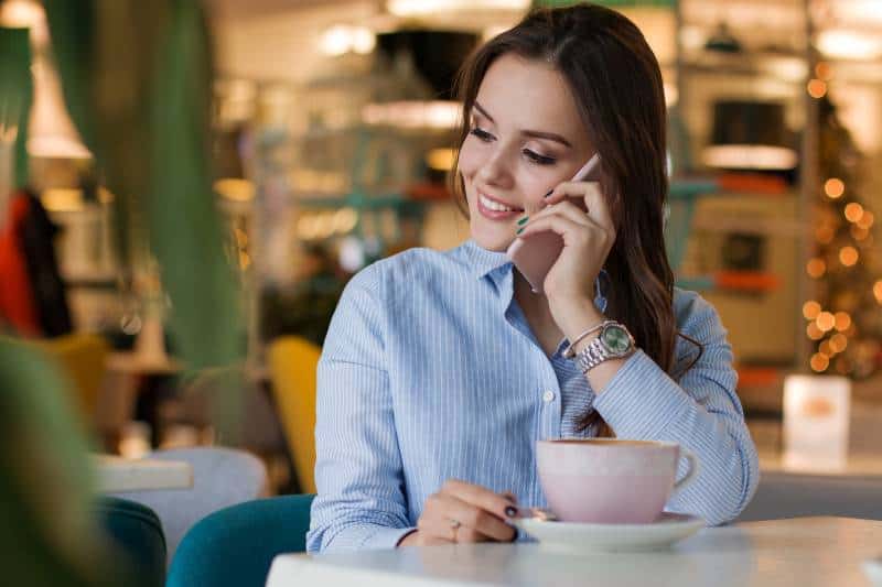 lächelndes Mädchen, das an ihrem Telefon im Café spricht