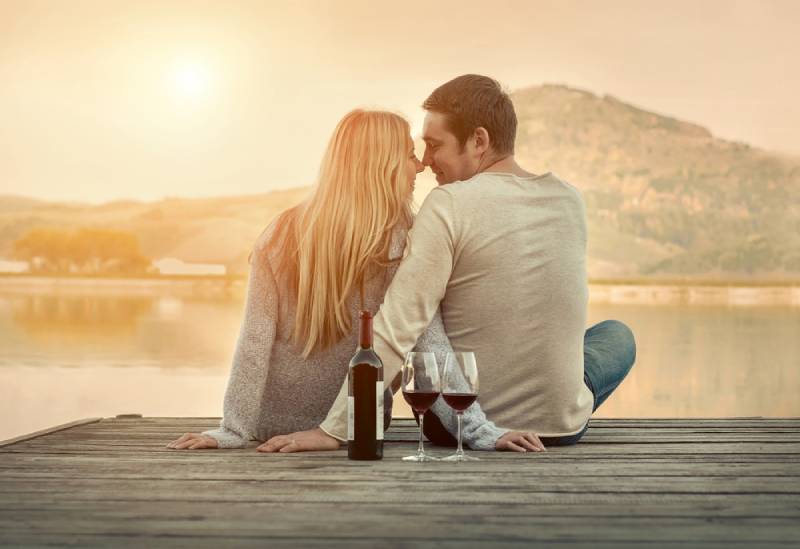 romantisches Paar, das vor See auf Sonnenuntergang sitzt