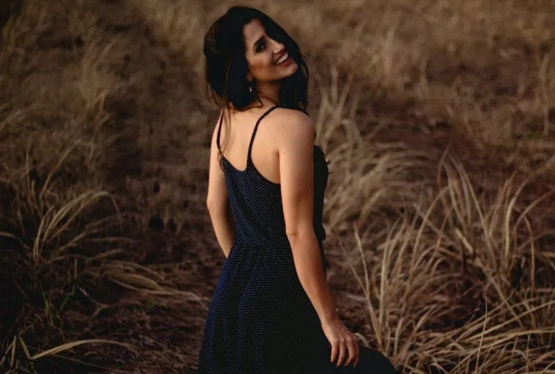 selektive Fokusfotografie der Frau im schwarzen Kleid, das am Grasfeld steht