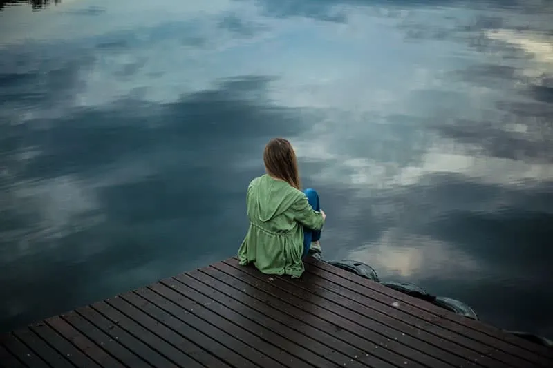 traurige Frau, die am See sitzt